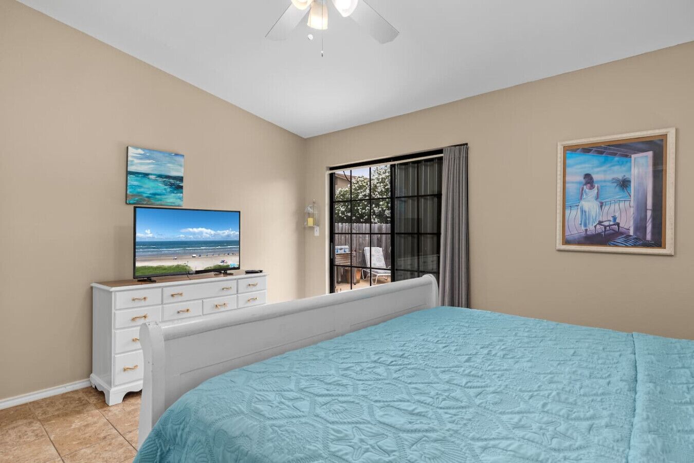 Een slaapkamer met een bed, een tv op een dressoir, een raam met gordijnen en een schilderij aan de muur.