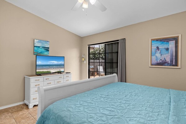 A bedroom with a bed, a TV on a dresser, a window with curtains, and a painting on the wall.