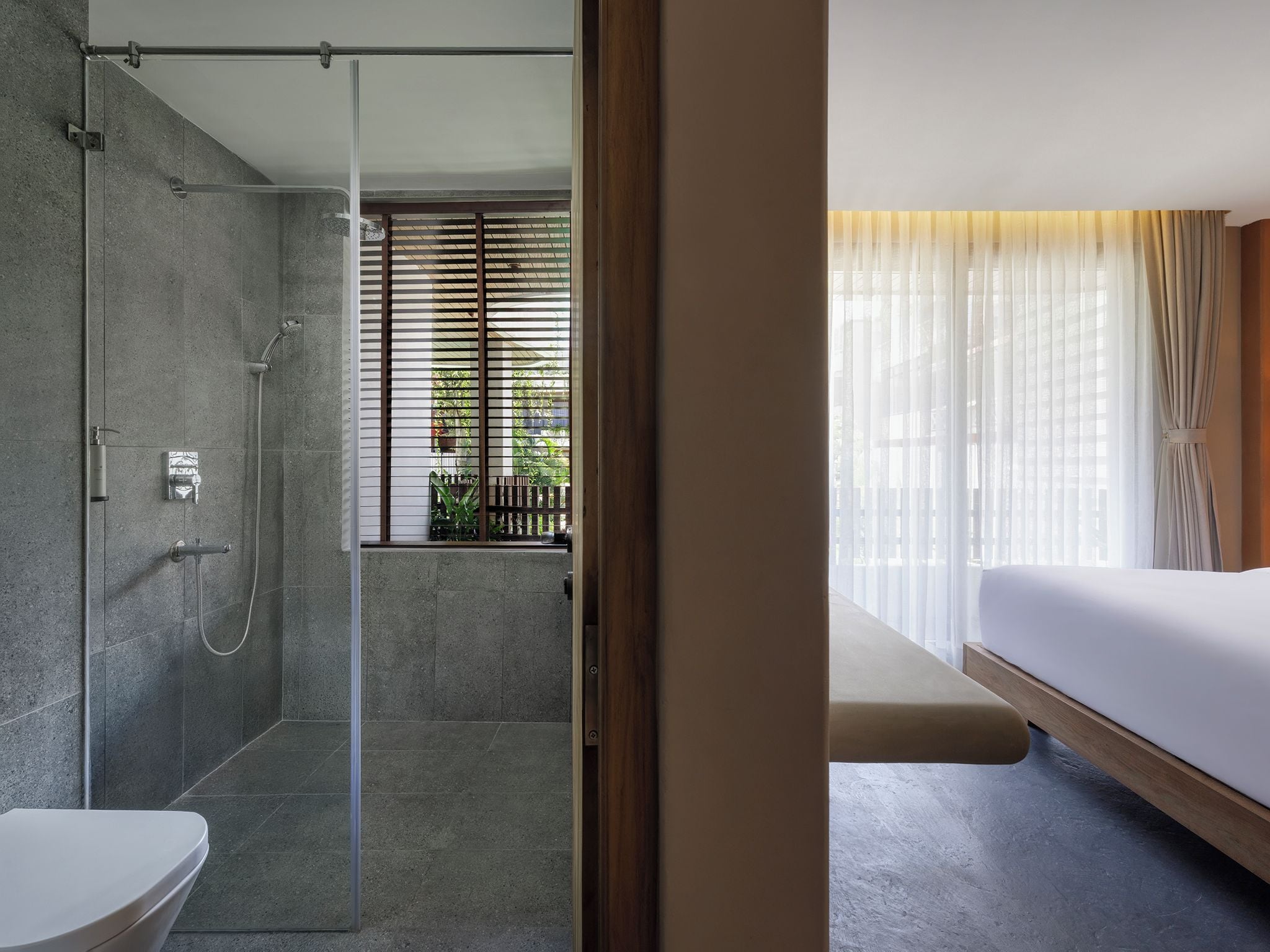 A modern bathroom with a glass shower enclosure, a toilet, and a window with blinds.