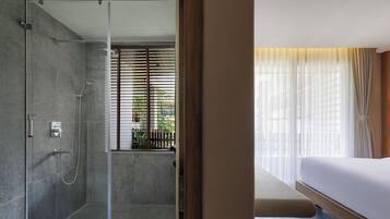 A modern bathroom with a glass shower enclosure, a toilet, and a window with blinds.