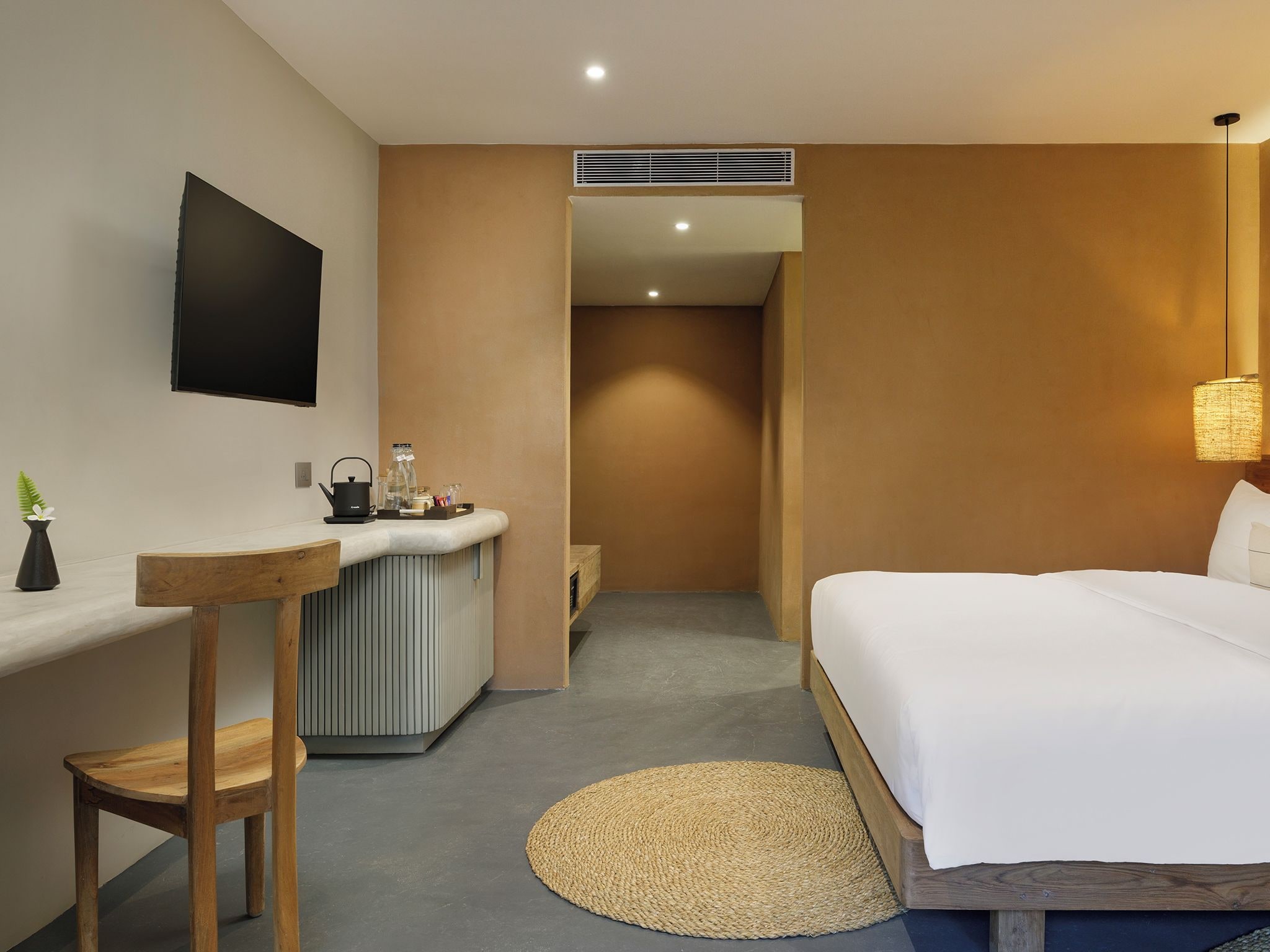 A hotel room with a bed, a desk, a chair, a small kitchenette, and a TV mounted on the wall.
