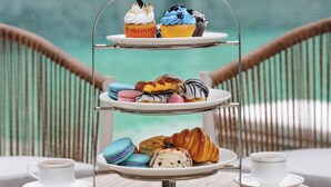 A three-tiered dessert stand with various pastries and a cup of tea on a round table. - Bagaincha Resort & Spa (Pokhara)