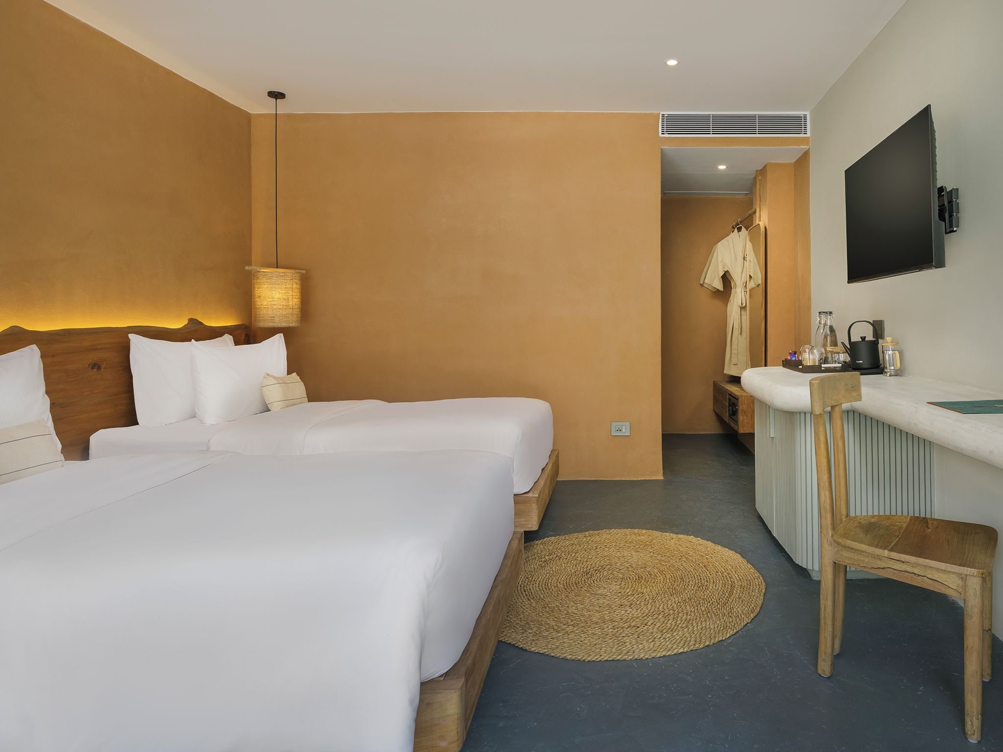 Une chambre d’hôtel avec deux lits, un bureau, une chaise, une télévision et une salle de bain visible au fond.