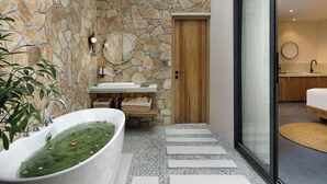 Un bagno moderno con parete in pietra, una vasca freestanding, una porta in legno e cabina doccia con pareti in vetro.