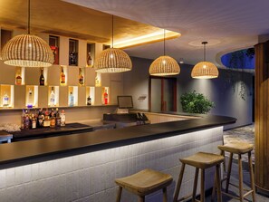 Uma área de bar com balcão, banquetas e luminárias pendentes.