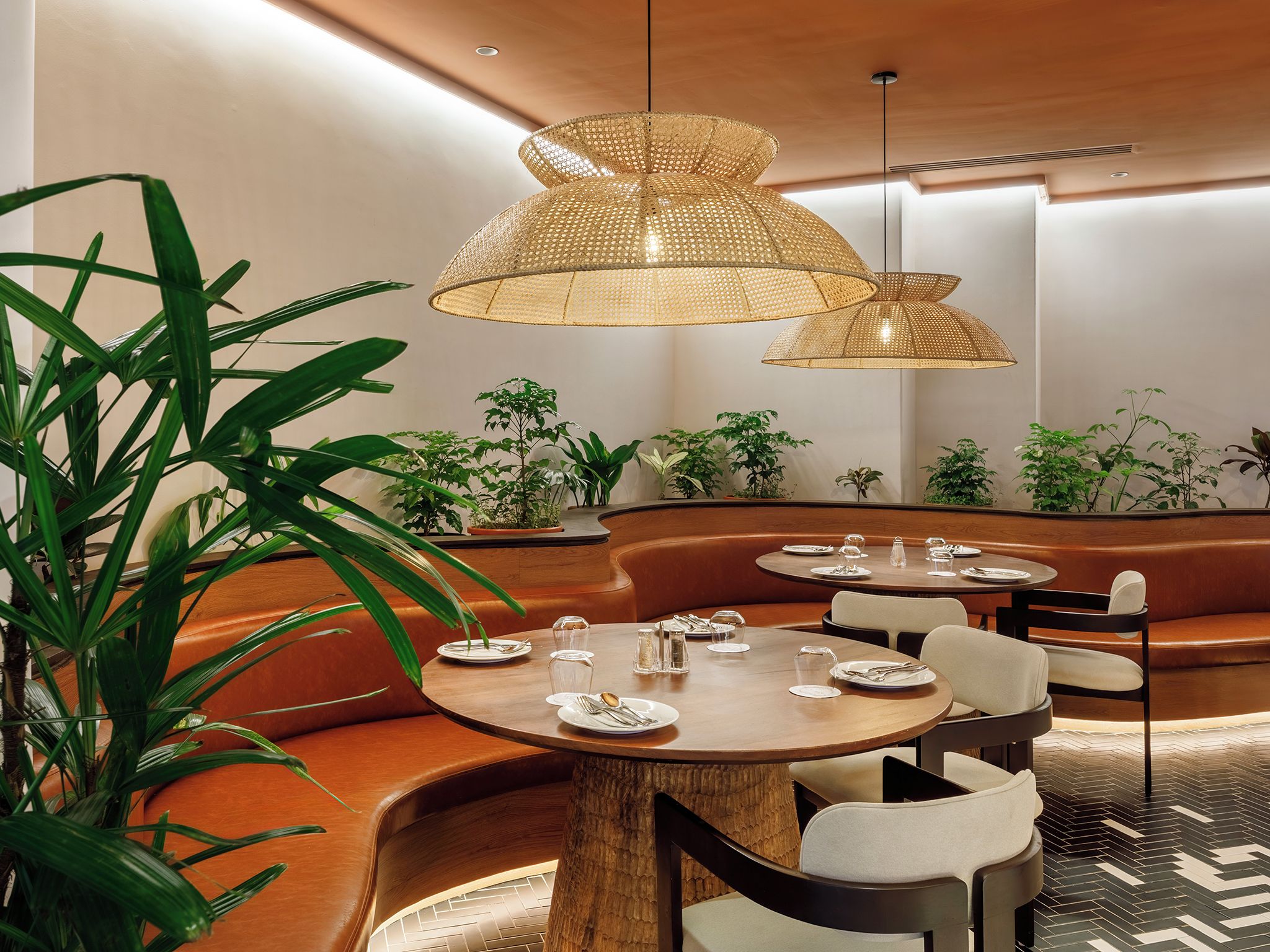 A modern dining area with round tables, cushioned seating, and hanging rattan lamps.