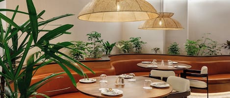 A modern dining area with round tables, cushioned seating, and hanging rattan lamps.