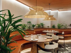 Un espace repas moderne avec des tables rondes, des sièges rembourrés et des lampes en rotin suspendues.