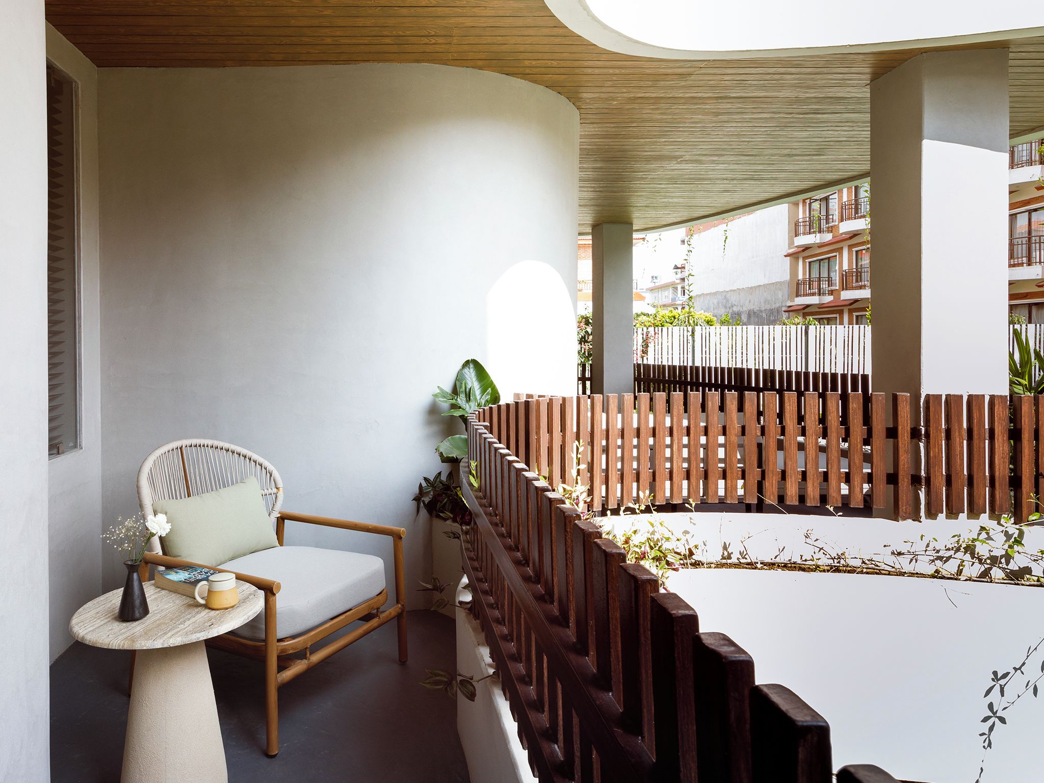 A balcony with a wooden fence, a wicker chair, and a small table with a vase and a book.