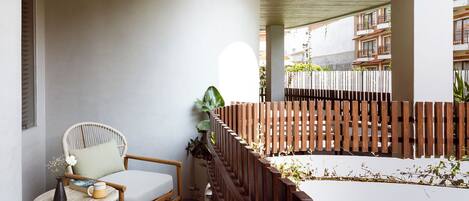Un balcón con cerramiento de madera, una silla de mimbre y una mesita con un jarrón y un libro.