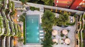 Vista aerea di una zona piscina su un tetto, con piscina, poltrone prendisole e vegetazione circostante.