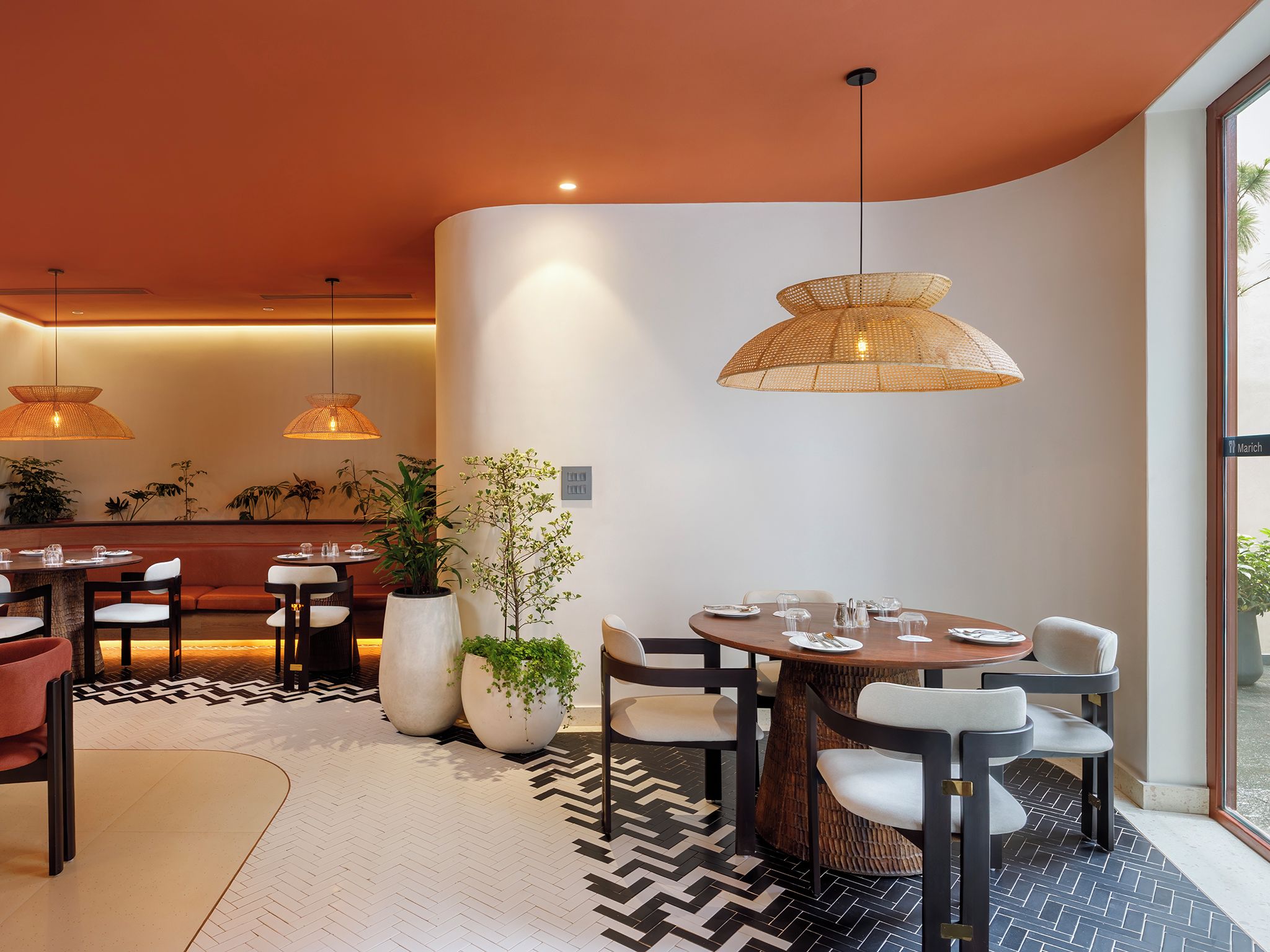 A modern dining area with round tables, chairs, and hanging rattan lamps.