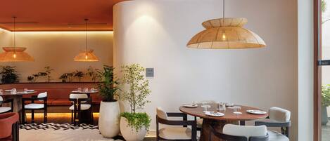 A modern dining area with round tables, chairs, and hanging rattan lamps.