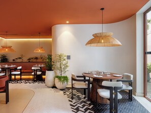 A modern dining area with round tables, chairs, and hanging rattan lamps. - Bagaincha Resort & Spa (Pokhara)