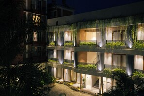 Um edifício com vários andares e varandas, algumas com plantas, e uma entrada bem iluminada.