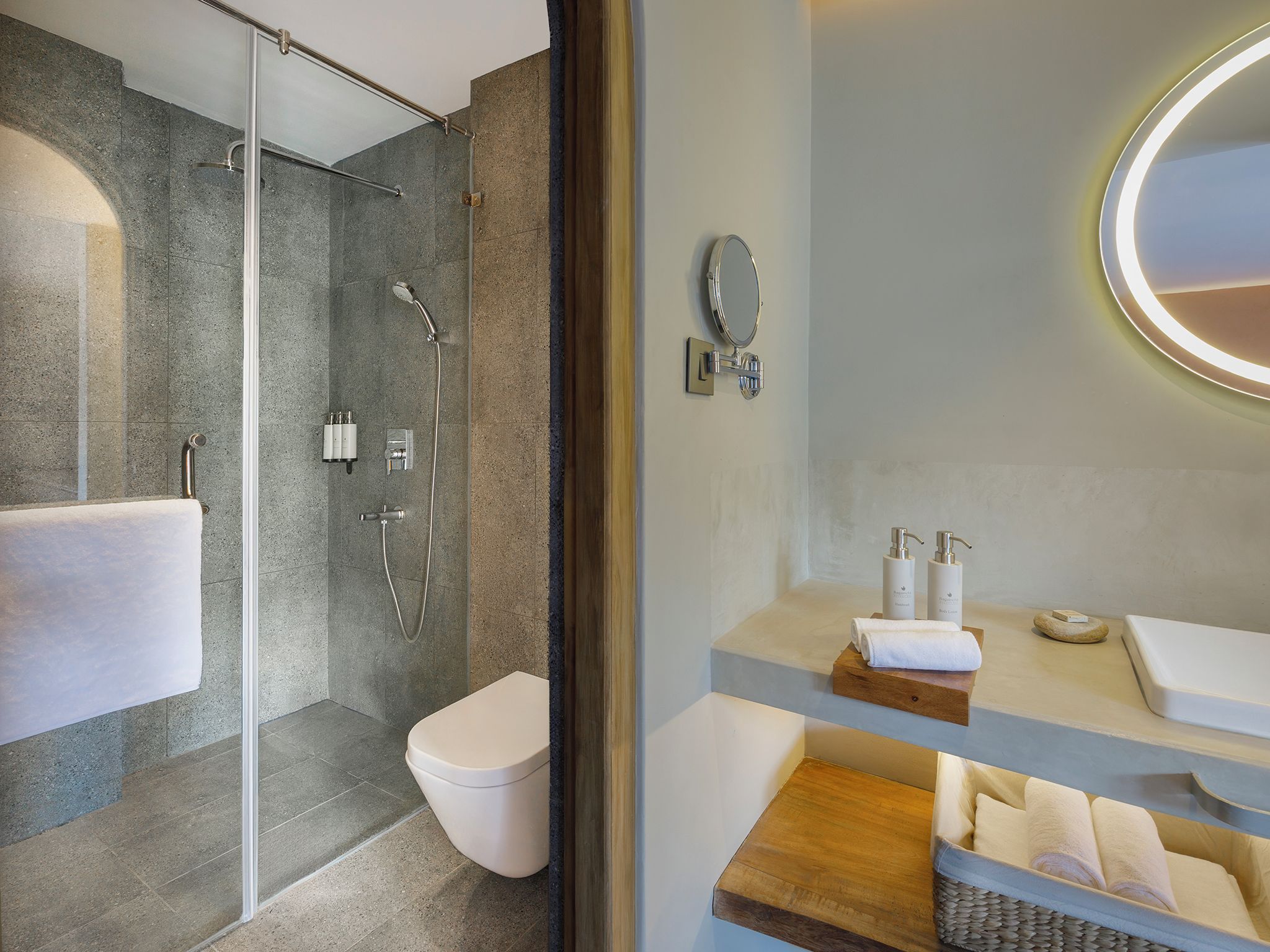 A modern bathroom with a glass-enclosed shower, a toilet, and a vanity with a mirror and toiletries.