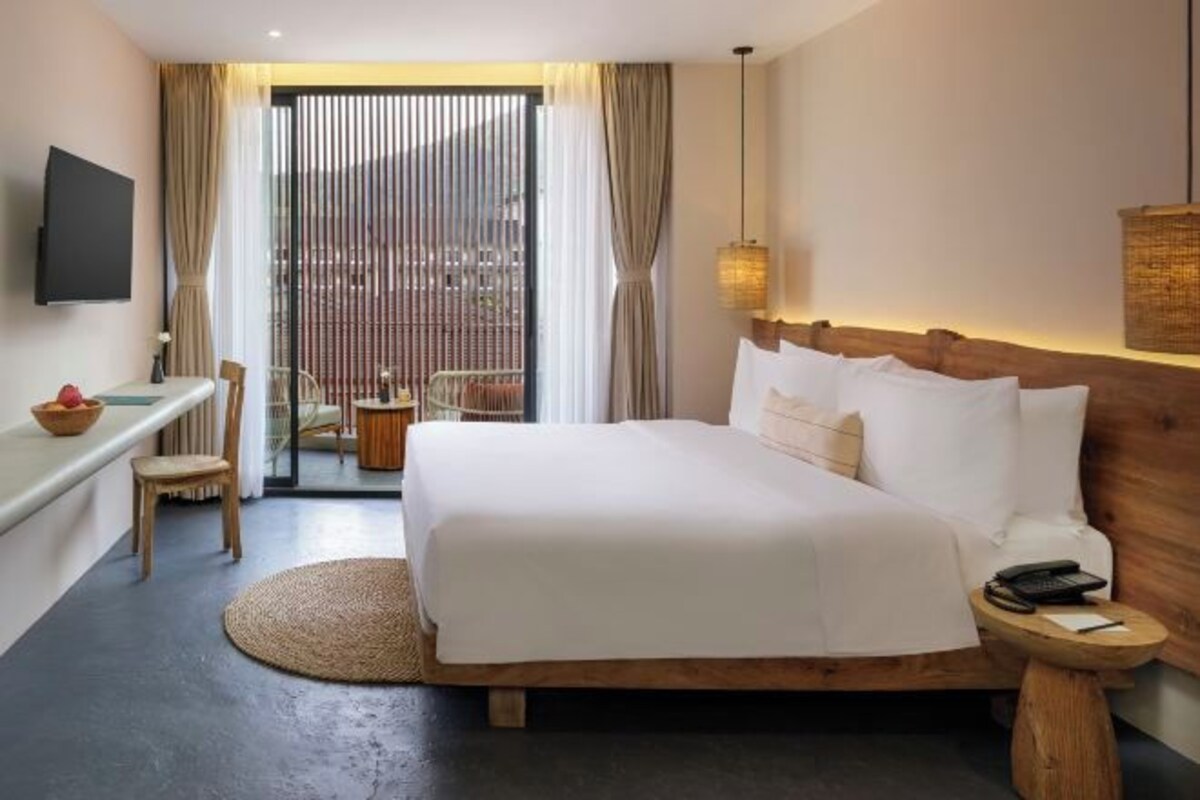 Habitación de hotel con cama, mesita de noche, silla y televisor en la pared.