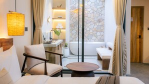 A modern hotel room with a seating area, a bathtub, and a view of a stone wall. - Bagaincha Resort & Spa (Pokhara)