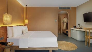 A hotel room with a large bed, bedside lamps, a desk with a flat-screen TV, a robe hanging, and a kitchenette.