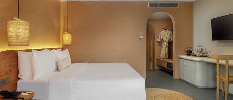 Habitación de hotel con una cama grande, lámparas de noche, un escritorio con televisor de pantalla plana, una bata colgada y una kitchenette.
