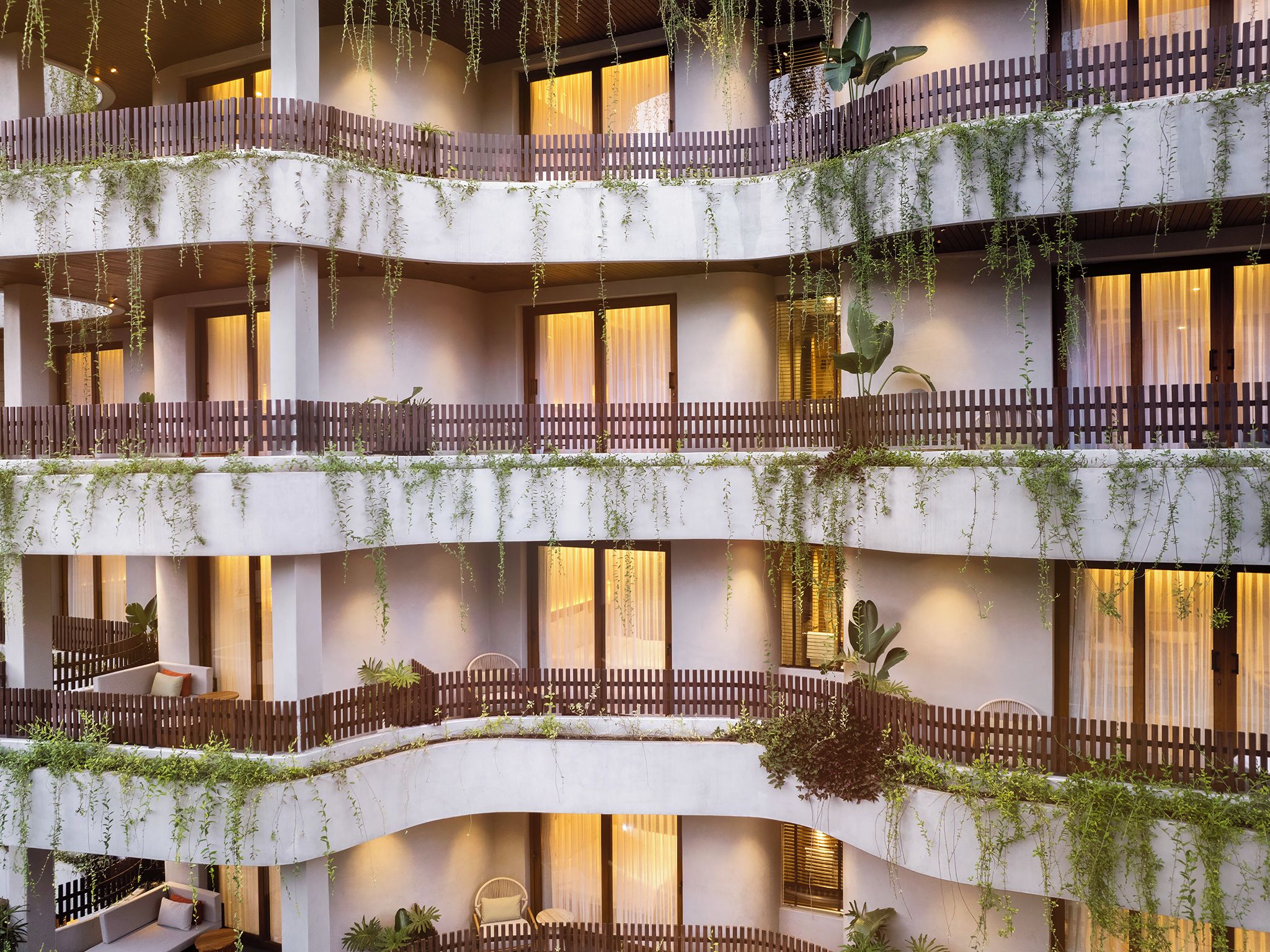 Un hotel de varios pisos con balcones, zonas de estar interiores y plantas.