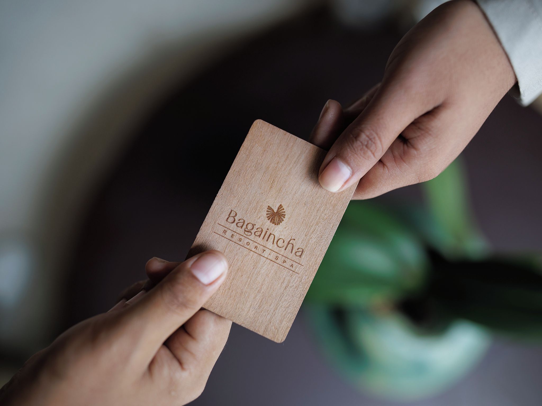 A hand holding a wooden card with the text 'Bagaincha Resort Spa' and a logo.