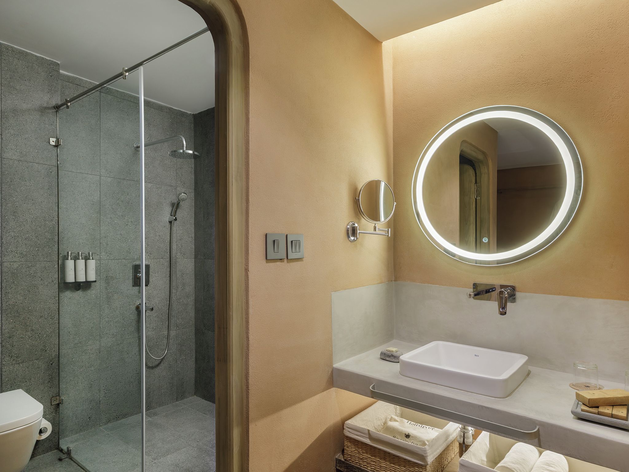 Un baño moderno con ducha de vidrio, un espejo redondo y un lavamanos blanco.