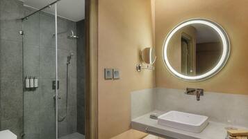Un baño moderno con ducha de vidrio, un espejo redondo y un lavamanos blanco.