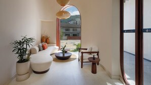 Un soggiorno moderno con un divano, un tavolino da caffè e poltrone, un'ampia finestra con vista sugli edifici, e un lampadario.