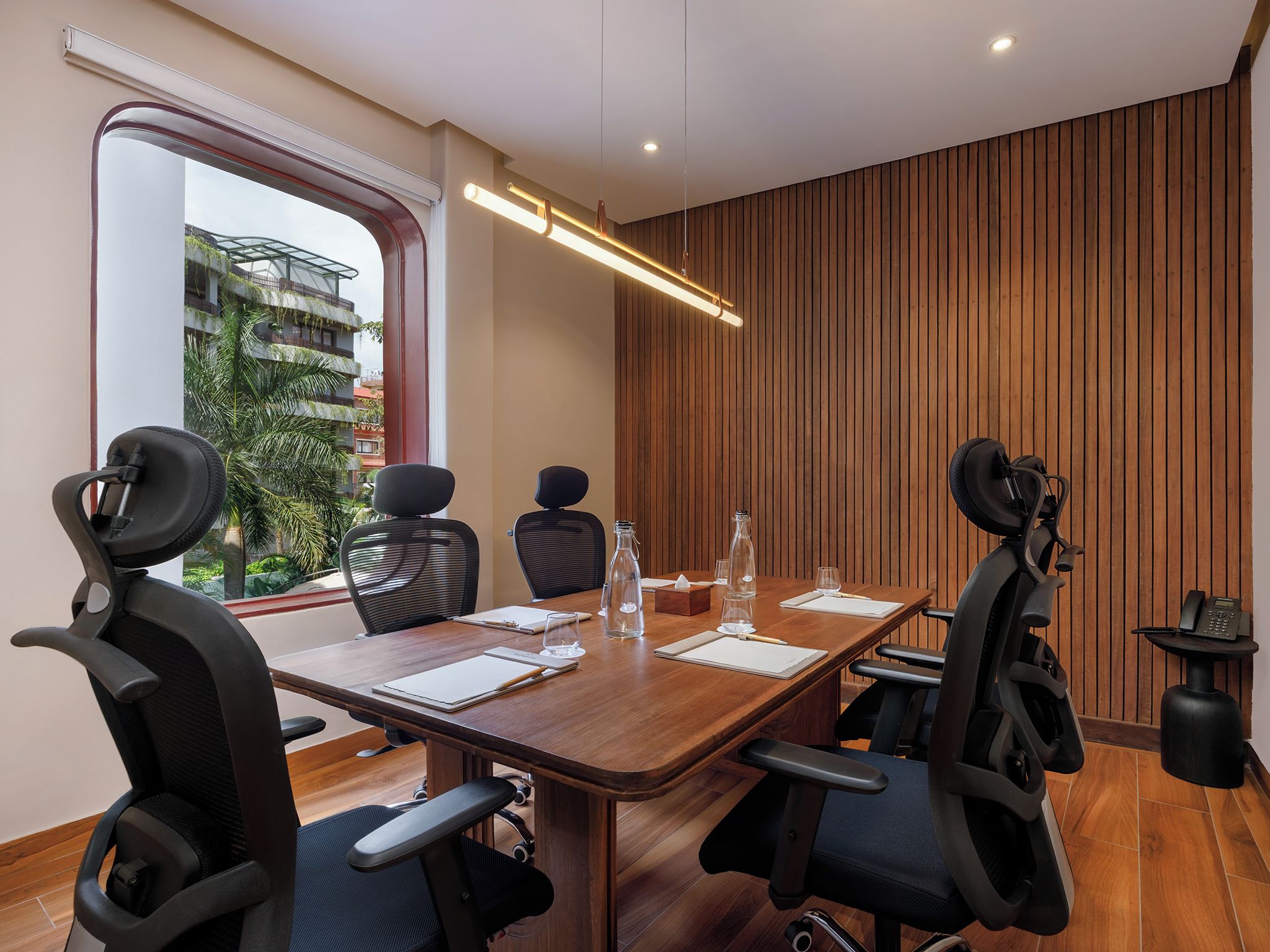 A conference room with a wooden table, four chairs, a large window, and a wooden wall panel.