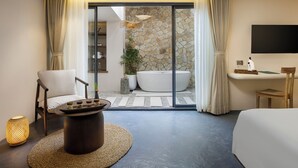 A modern bedroom with a large bed, a sitting area with a coffee table, a bathtub, and a TV mounted on the wall. - Bagaincha Resort & Spa (Pokhara)