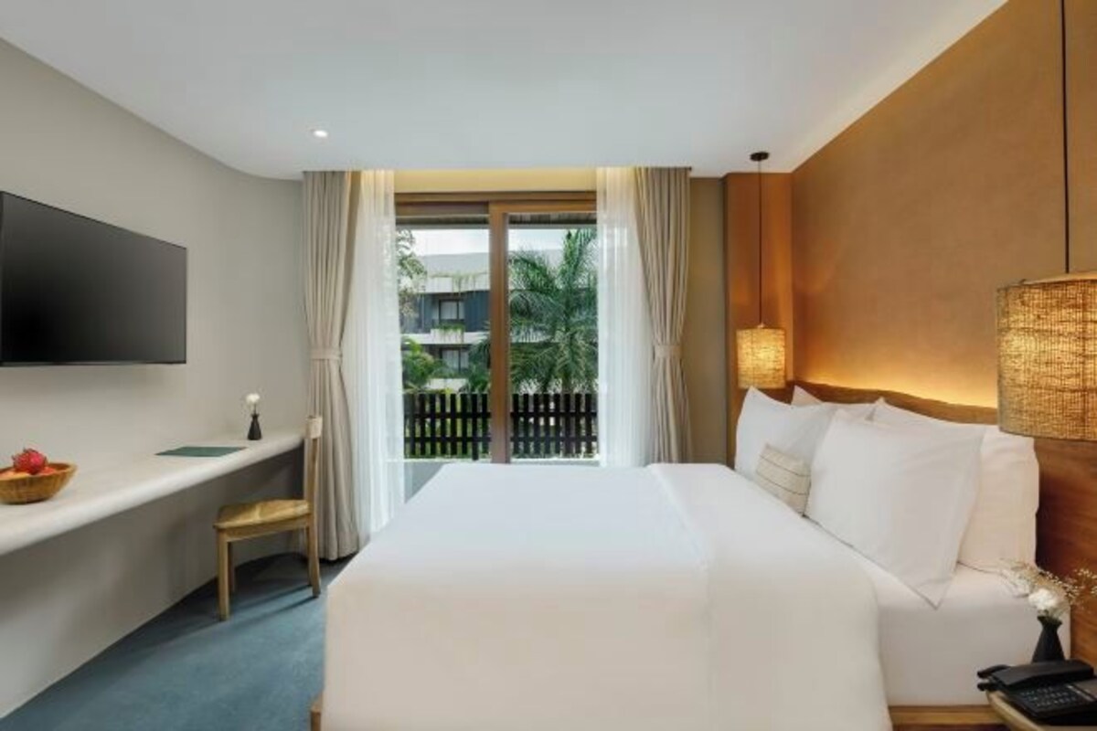 Habitación de hotel con cama, escritorio, televisor de pantalla plana, lámpara y vista al exterior.