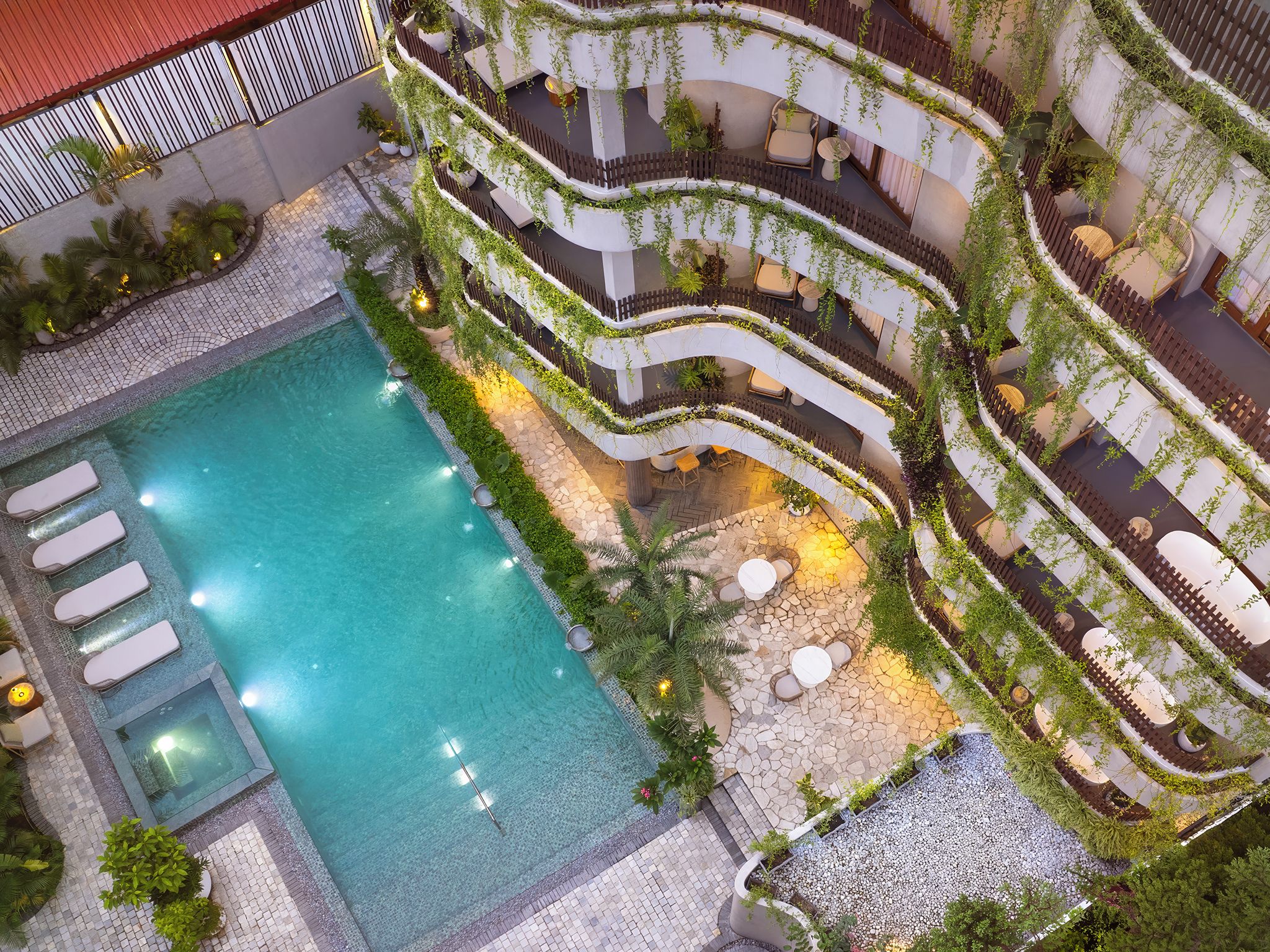 Uma área de piscina em vários níveis, com uma piscina central, rodeada por terraços com assentos e vegetação.