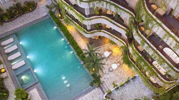 Uma área de piscina em vários níveis, com uma piscina central, rodeada por terraços com assentos e vegetação.
