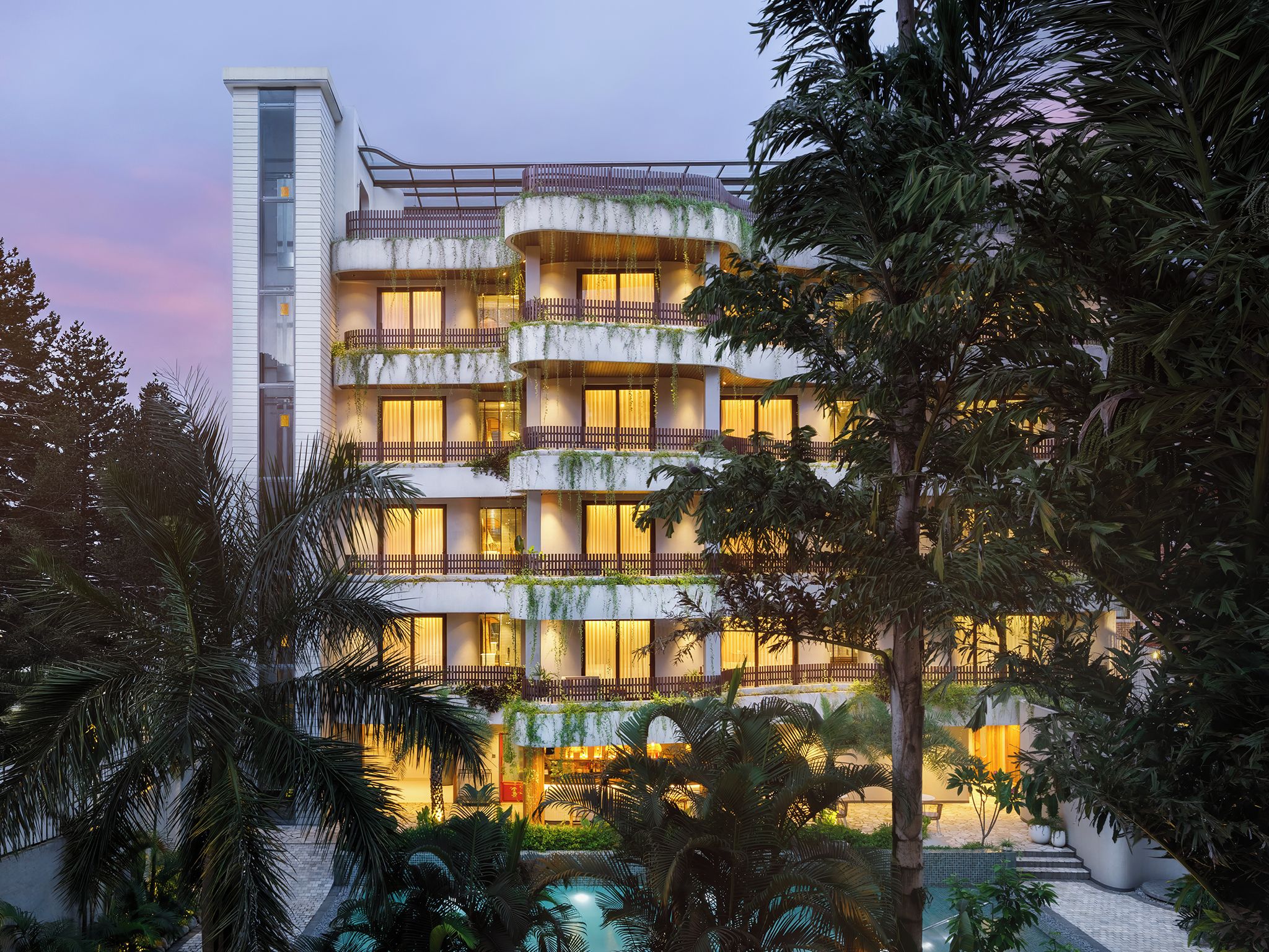 A multi-story hotel with balconies, a pool, and lush greenery.
