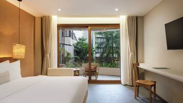 Hotelkamer met een bed, bureau, stoel, televisie en balkon met uitzicht op groen en gebouwen.