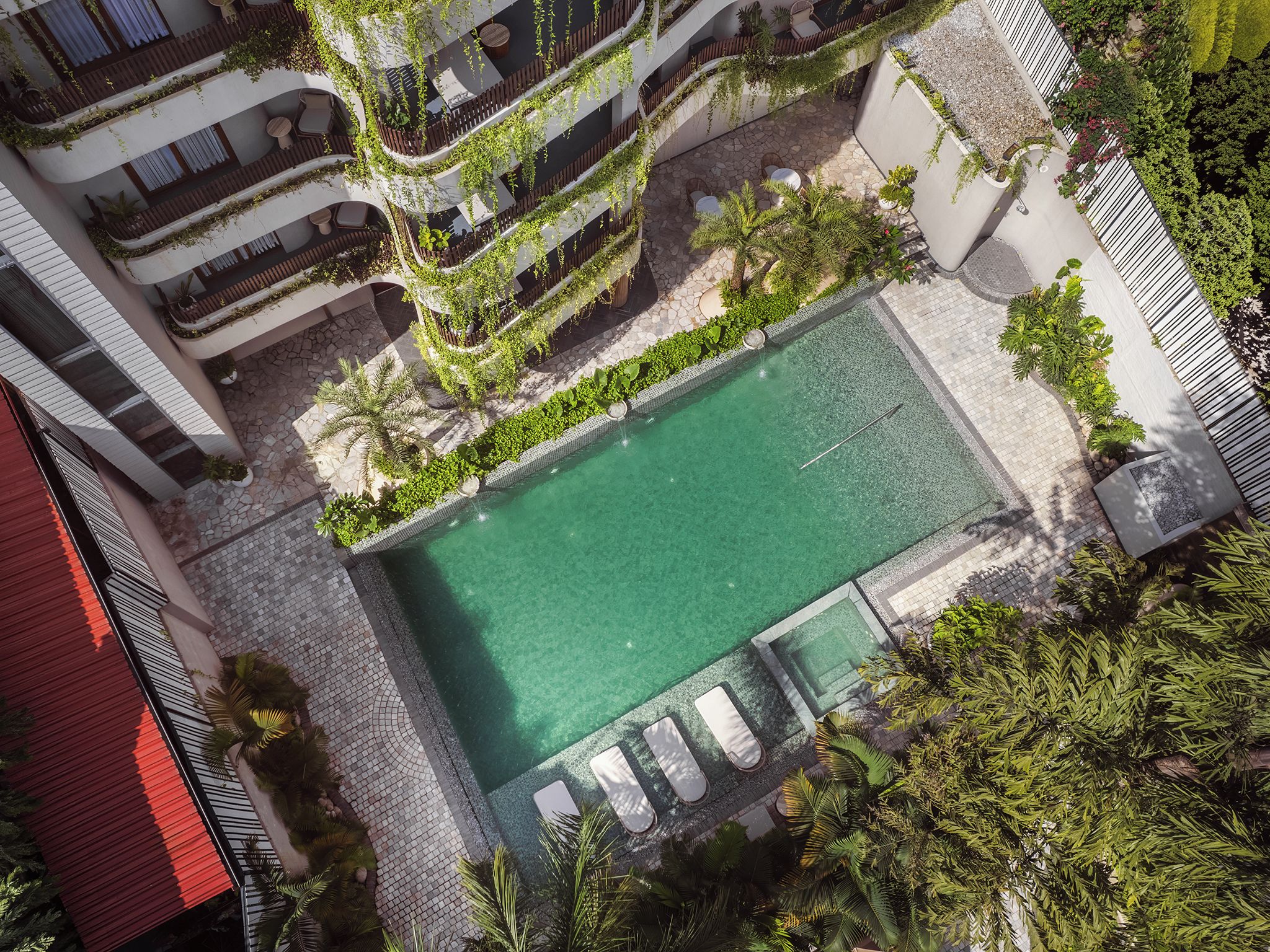 Luchtbeeld van een hotel met een zwembad, omgeven door groen en een pad van stenen.