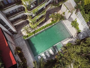 Vista aérea de un hotel con piscina, rodeado de vegetación y un camino de piedra.