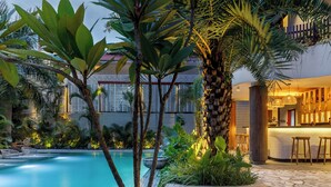 Una piscina con un vialetto in pietra, circondata da piante tropicali e un'area bar in legno.