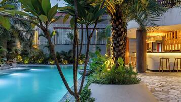 Una piscina con un sendero de piedra, rodeada de plantas tropicales y una zona de bar de madera.