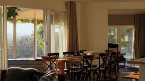 Una sala de estar moderna con un ventanal grande, un comedor con mesa y sillas, y una zona de estar acogedora con un sofá y una butaca.