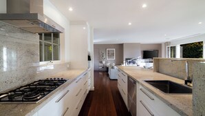 Una cocina moderna con estufa a gas, armarios blancos, una campana extractora de acero inoxidable y una isla grande con pileta.