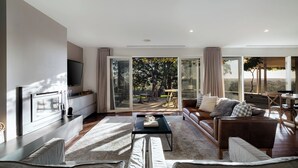 Una sala de estar moderna con sofá, mesa de centro y televisor. Hay una puerta corrediza de vidrio que da a un patio con mobiliario exterior.