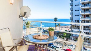 Un balcón con una mesa de vidrio, una silla, una planta en maceta y vista a la playa y al océano.
