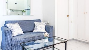 Una habitación con un sofá azul a cuadros, una mesa de centro de vidrio y una puerta blanca.