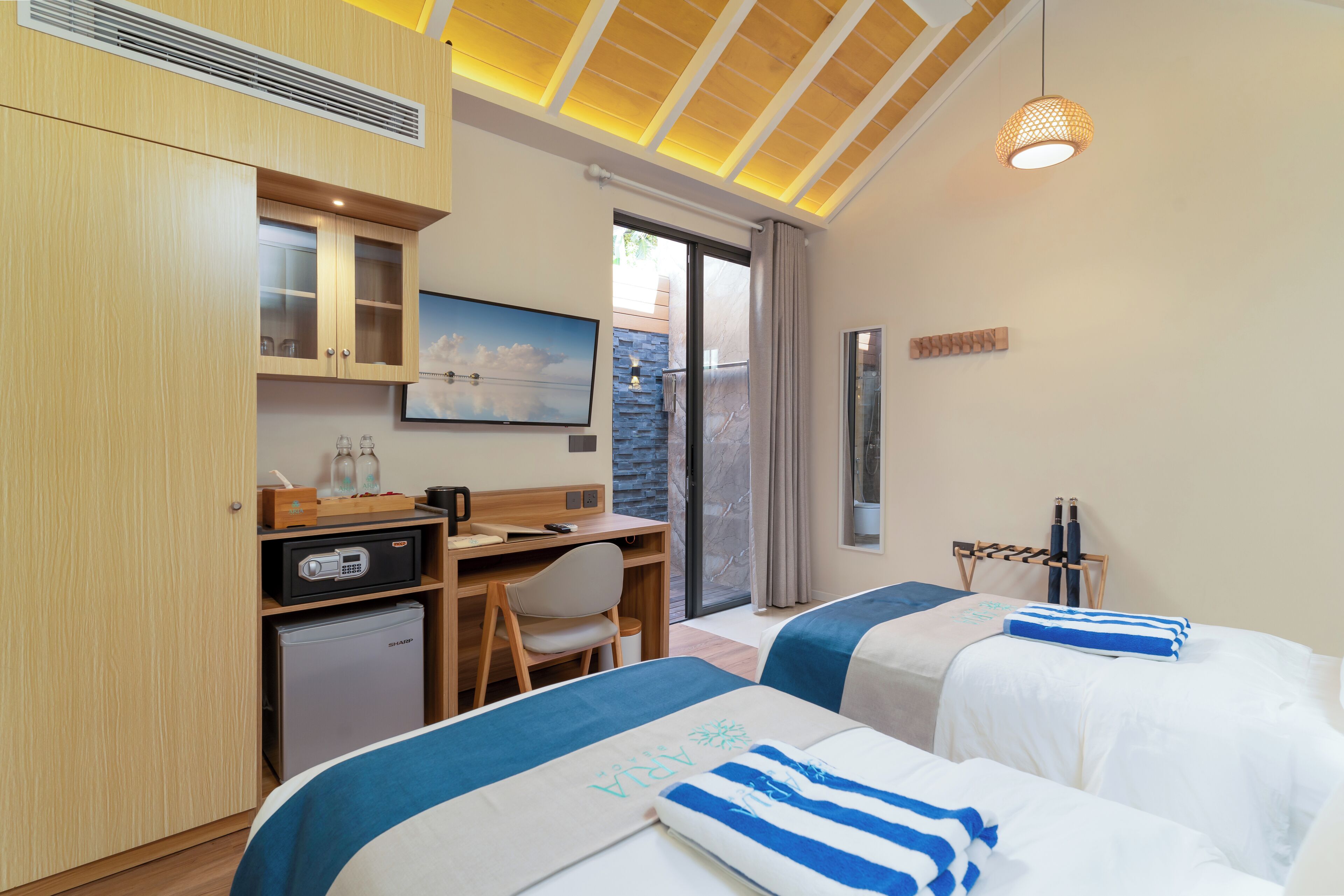 Habitación de hotel con dos camas, un escritorio, un refrigerador pequeño, un televisor y vistas al exterior a través de una puerta corrediza.