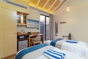 Habitación de hotel con dos camas, un escritorio, un refrigerador pequeño, un televisor y vistas al exterior a través de una puerta corrediza.