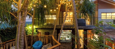 A modern building with a wooden deck, string lights, and tropical plants.
