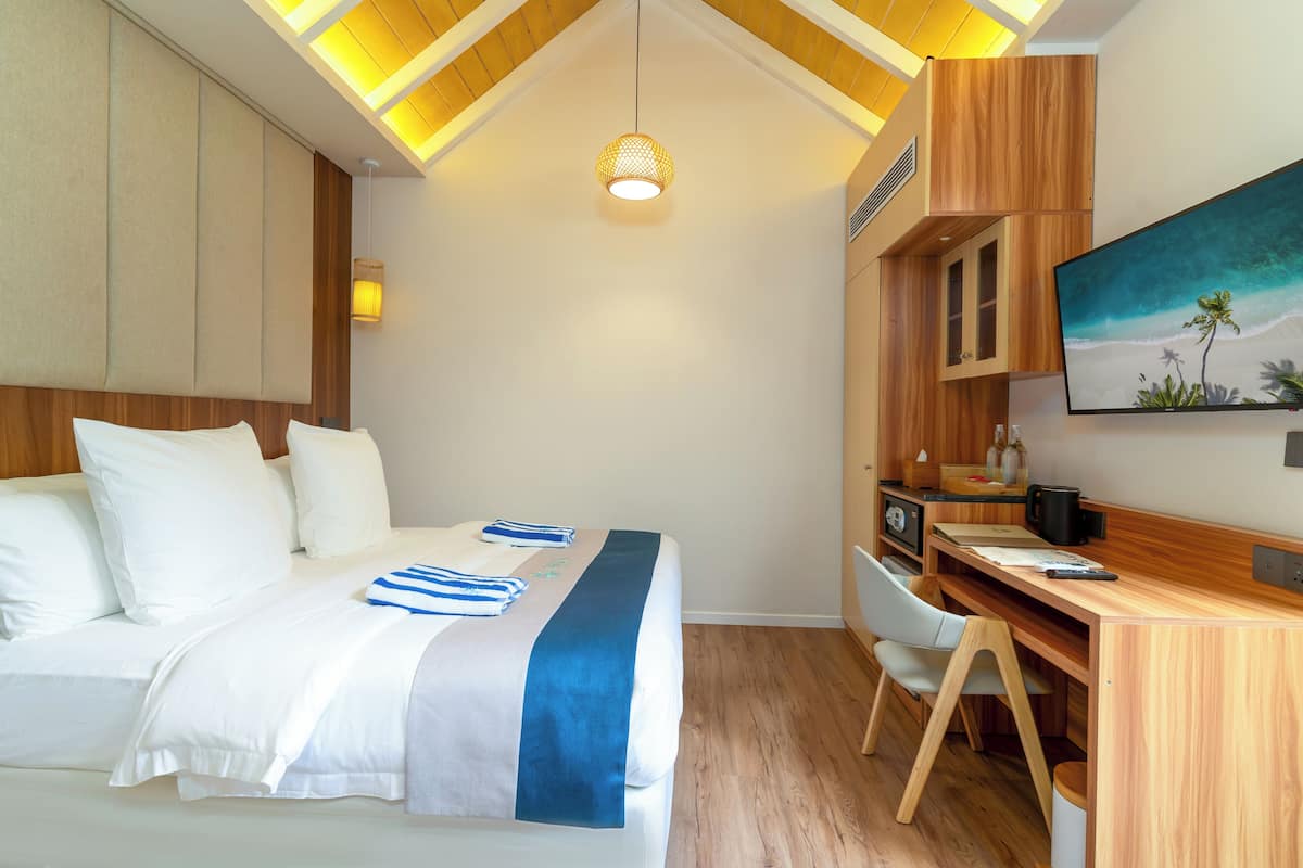 A hotel room with a bed, a desk, and a painting of a beach scene.