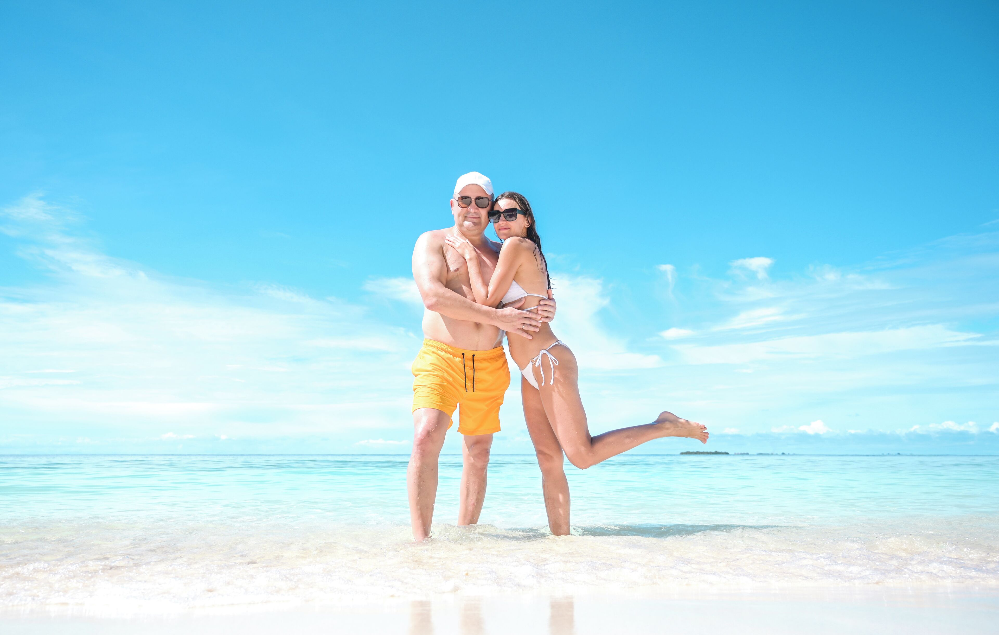 Una pareja abrazándose en una playa con cielos despejados y aguas tranquilas.